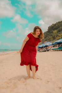 Young woman wearing red dress while standing at beach