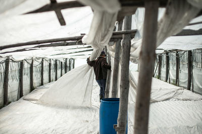 Rear view of man arranging fabric in shed