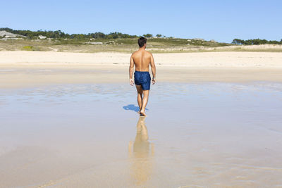 Back view of shirtless man walking on beach