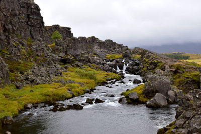 Stream flowing through rocks against sky