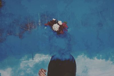 Woman wearing flowers while standing amidst blue smoke