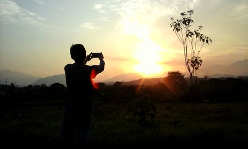 Rear view of silhouette man photographing on field at sunset