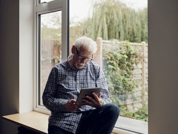 Senior man by the window at home using digital tablet