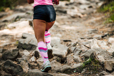 Female runner in pink compression socks running uphill in woods