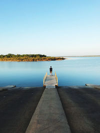 Rear view of man standing on jetty over sea against clear sky
