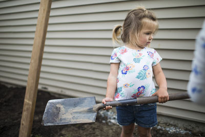 Cute girl holding shovel in backyard.