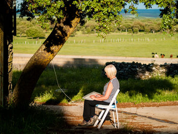 Woman typing in keyboard while sitting on chair against trees