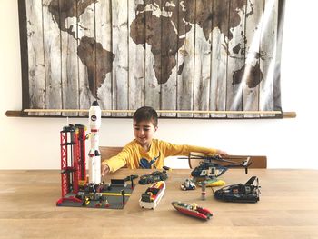 Boy playing with toys on table against world map at home