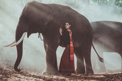 Full length of smiling woman standing with elephant in forest