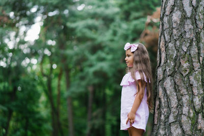 Beautiful girl in a pink dress stands near a tree in the forest and dreams