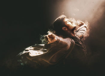 Digital composite image of light falling on man with arms outstretched amidst smoke