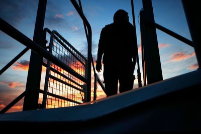 Rear view of silhouette man on railing against sky