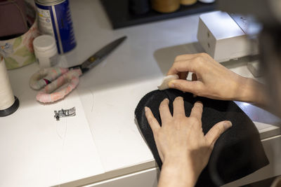 Woman is sewing black beanie hat on a sewing machine, using a sewing machine on the sewing table