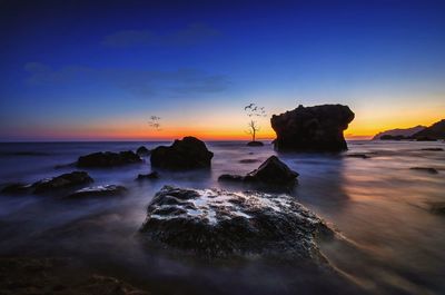 Rocks on beach against sky during sunset