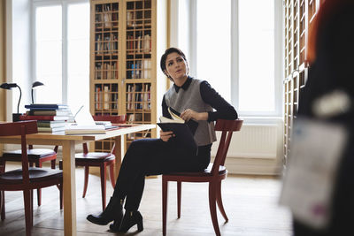 Female lawyer holding book while looking up in library