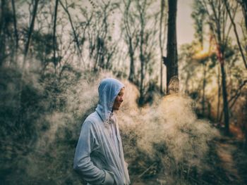 Man standing by tree trunk in forest