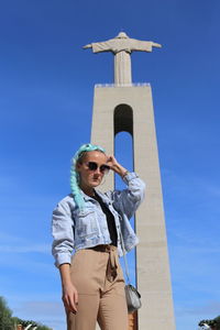 Low angle view of man wearing sunglasses standing against blue sky