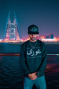 Portrait of smiling man standing by river against clear sky at night