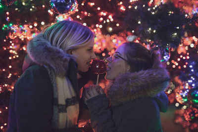 Female friends holding caramelized apple during christmas at night