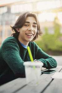 Portrait of happy teenager leaning at table outdoors