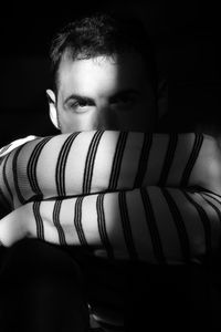 Portrait of young man sitting against black background