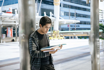 Side view of young man reading book while standing in city