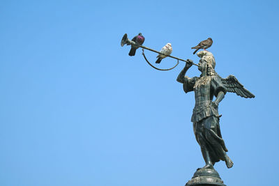 Low angle view of birds perching on statue against clear blue sky