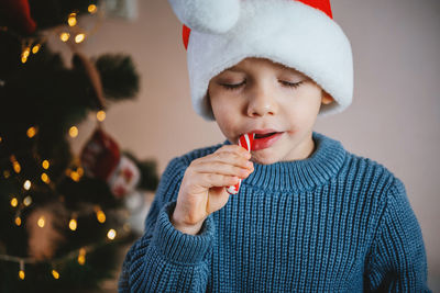 Little girl in eyeglasses and santa hat eating candy cane lollipop lo at christmas time