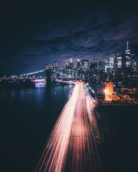 Light trails on street by illuminated buildings against sky at night