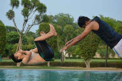 Boys jumping in swimming pool against sky