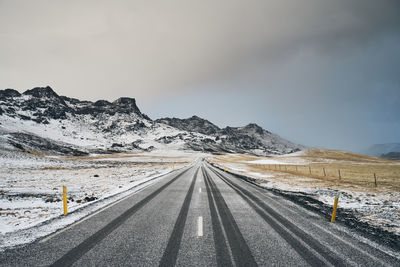 Road leading towards snowcapped mountains against sky