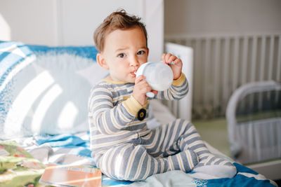 Cute adorable caucasian kid boy sitting on bed drinking milk from kids bottle. healthy eating. 