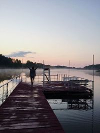 Rear view of silhouette man standing on pier at lake against sky