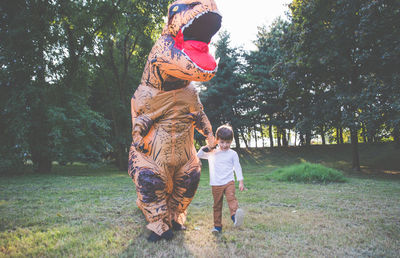 Boy walking with person wearing dinosaur costume in park