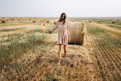 Smiling woman in sunglasses with bare shoulders on a background of wheat field and bales of hay.