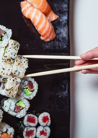 Top view of woman's hand holding sushi sticks. sushi rolls laid out. vertical picture