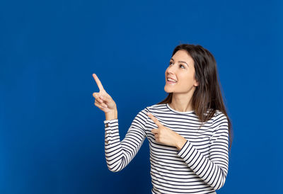 Young woman gesturing while standing against blue background