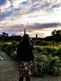 Rear view of woman standing against plants during sunset