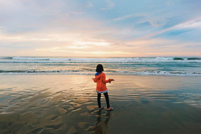 Rear view of man standing on beach against sky during sunset