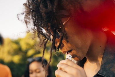 Close-up of young man with curly hair smoking through electronic cigarette