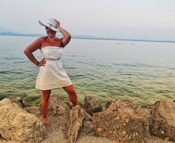 Woman wearing hat standing on rock by sea against sky