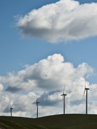 Low angle view of windmills on hill against cloudy sky