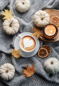 White pumpkins, coffee and autumn leaves on a grey knitted sweater. autumn home decor.