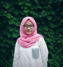 Portrait of young woman in hijab standing against pink plants