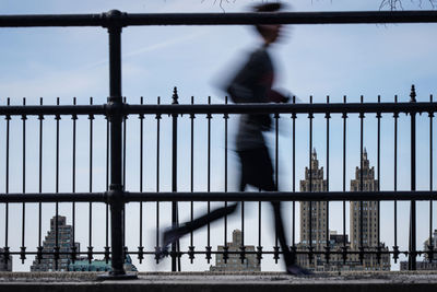 Side view of man running on bridge against buildings in city