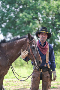Portrait of senior cowboy standing with horse on land