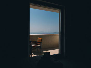 Chair in balcony against sky seen from glass at home