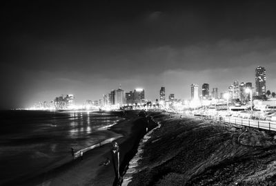 People at beach in illuminated city at night