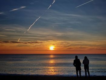 Silhouette people on beach against sky during sunset