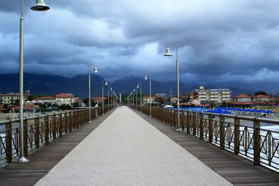 Illuminated street light by railing against sky